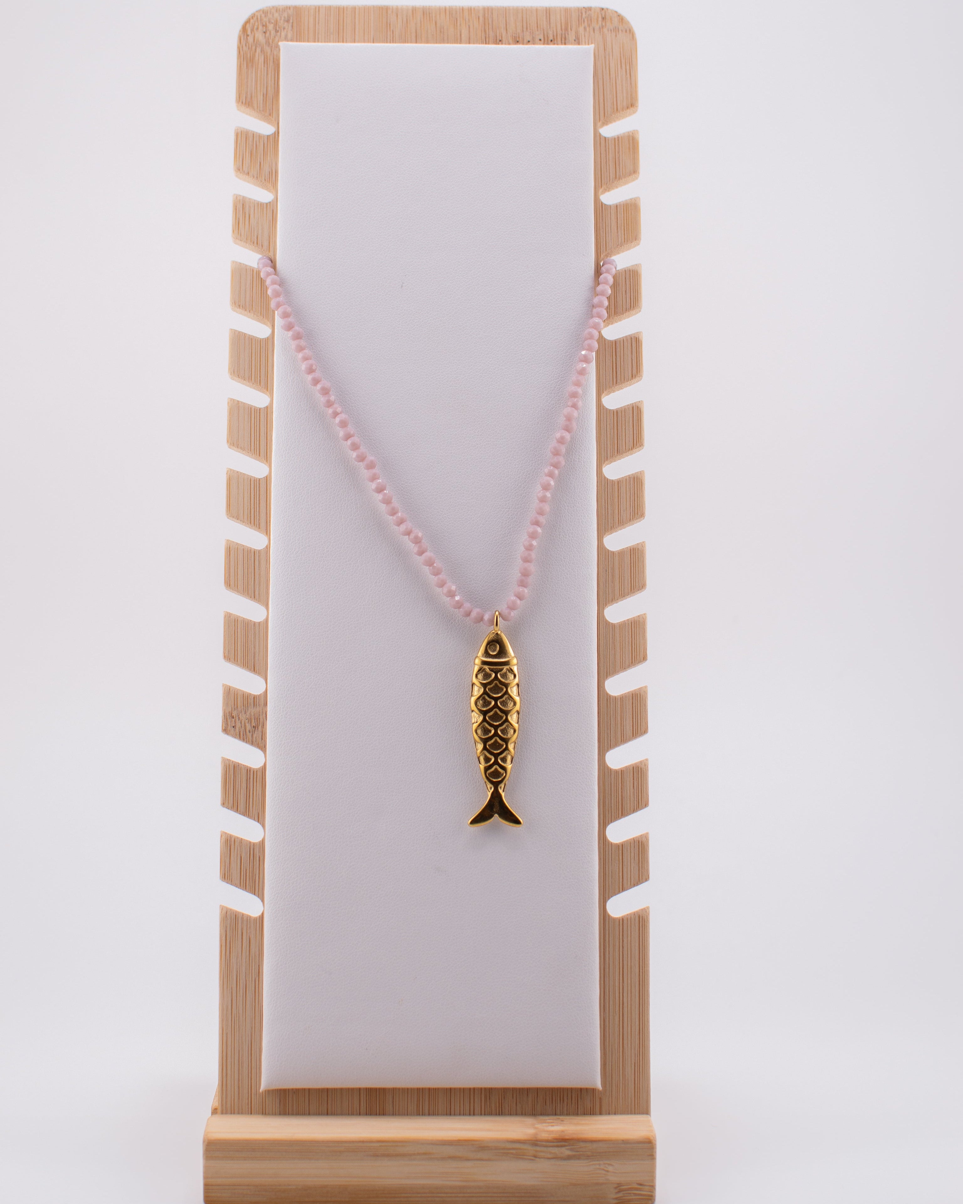Necklace with a fish pendant on a striped stand against a white background