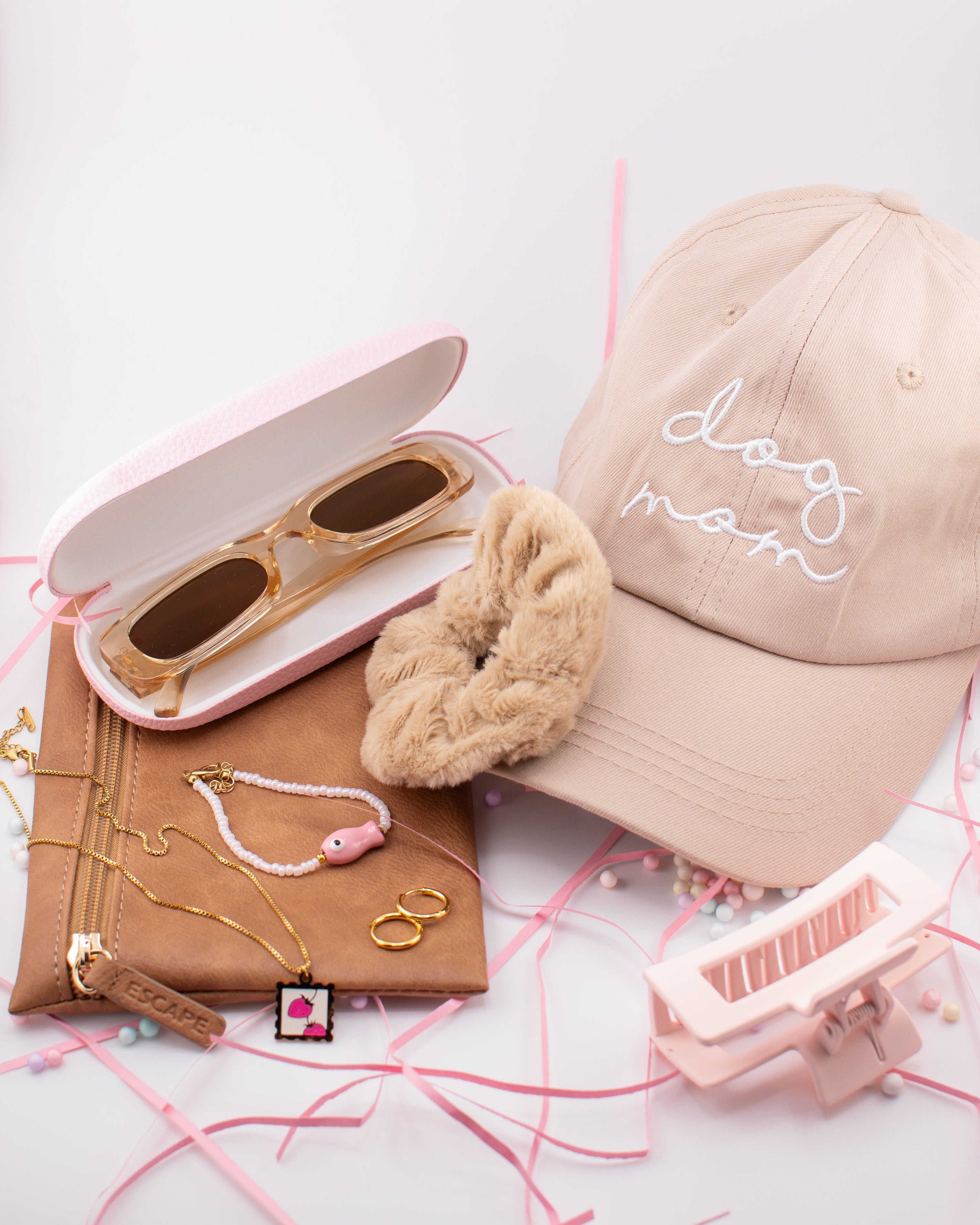 Beige cap with 'dog mom' embroidery, sunglasses, scrunchie, and accessories on a white background